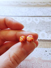 Load image into Gallery viewer, A pair of red and yellow stud earrings held between finger and thumb