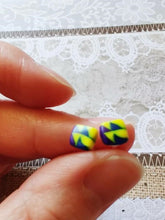 Load image into Gallery viewer, Two stud earrings held between finger and thumb composed of yellow, blue, and purple triangles