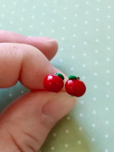 Load image into Gallery viewer, A pair of miniature apple stud earrings held between finger and thumb