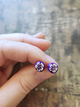 Load image into Gallery viewer, White and gold flowers on a purple background stud earrings held between finger and thumb
