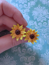 Load image into Gallery viewer, Two 3/4 inch sunflower earring studs held between finger and thumb