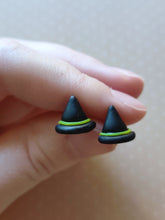 Load image into Gallery viewer, A pair of black witches hats with yellow bands made into flat backed stud earrings. Earrings are displayed between finger and thumb.