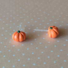 Load image into Gallery viewer, A pair of flat backed, side view, orange pumpkin earrings sitting on pastel orange and white polka dot paper.