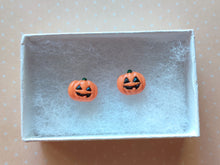 Load image into Gallery viewer, A pair of flat backed jack o' lantern earrings with relief sculpted detail and painted on face and stem. The earrings are inside a white paper jewelry box.
