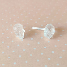 Load image into Gallery viewer, One pair of clear skull stud earrings displayed on a pale orange and white polka dot background.