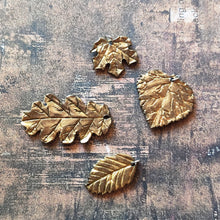 Load image into Gallery viewer, A group of polymer clay leaves showing a gold finish similar to plaited or brushed gold. The leaves are shaped like one leaf each of a red maple, oak, beach, and aspen leaf.