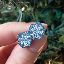 Load image into Gallery viewer, Two hexagon shaped earrings with a kaleidoscope pattern reminiscent of a snowflake or stained glass. the earrings are held between finger and thumb in front of an artificial Christmas tree branch.
