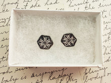 Load image into Gallery viewer, Two hexagon shaped earrings with a kaleidoscope pattern reminiscent of a snowflake or stained glass. The earrings are inside a white paper jewelry box.