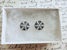Load image into Gallery viewer, Two hexagon shaped earrings with a snowflake pattern in silver and white. The earrings are inside a white paper jewelry box.