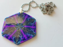 Load image into Gallery viewer, A large hexagonal pendant connected to a silver colored chain and bail. The pendent is dark blue with purple, gold, and light blue colors radiating out from the center. It is displayed laying on a white plain ceramic tile.