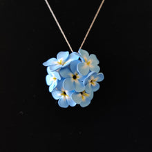 Load image into Gallery viewer, A large pendant hanging from a silver colored chain displayed on a black velvet background. The pendant is a round cluster of seven Forget Me Not imitation flowers made of polymer clay. Each of the flower petals is blue at the edges, fades to white, and ends in yellow in the middle. The center of the flowers is black.