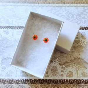 Two miniature pumpkin stud earrings inside a white paper jewelry box