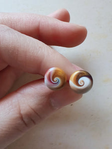 Purple, gold and white swirl earrings held between finger and thumb