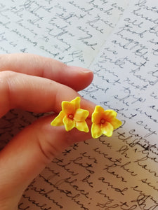 One pair of yellow and orange daylily earrings held between finger and thumb.