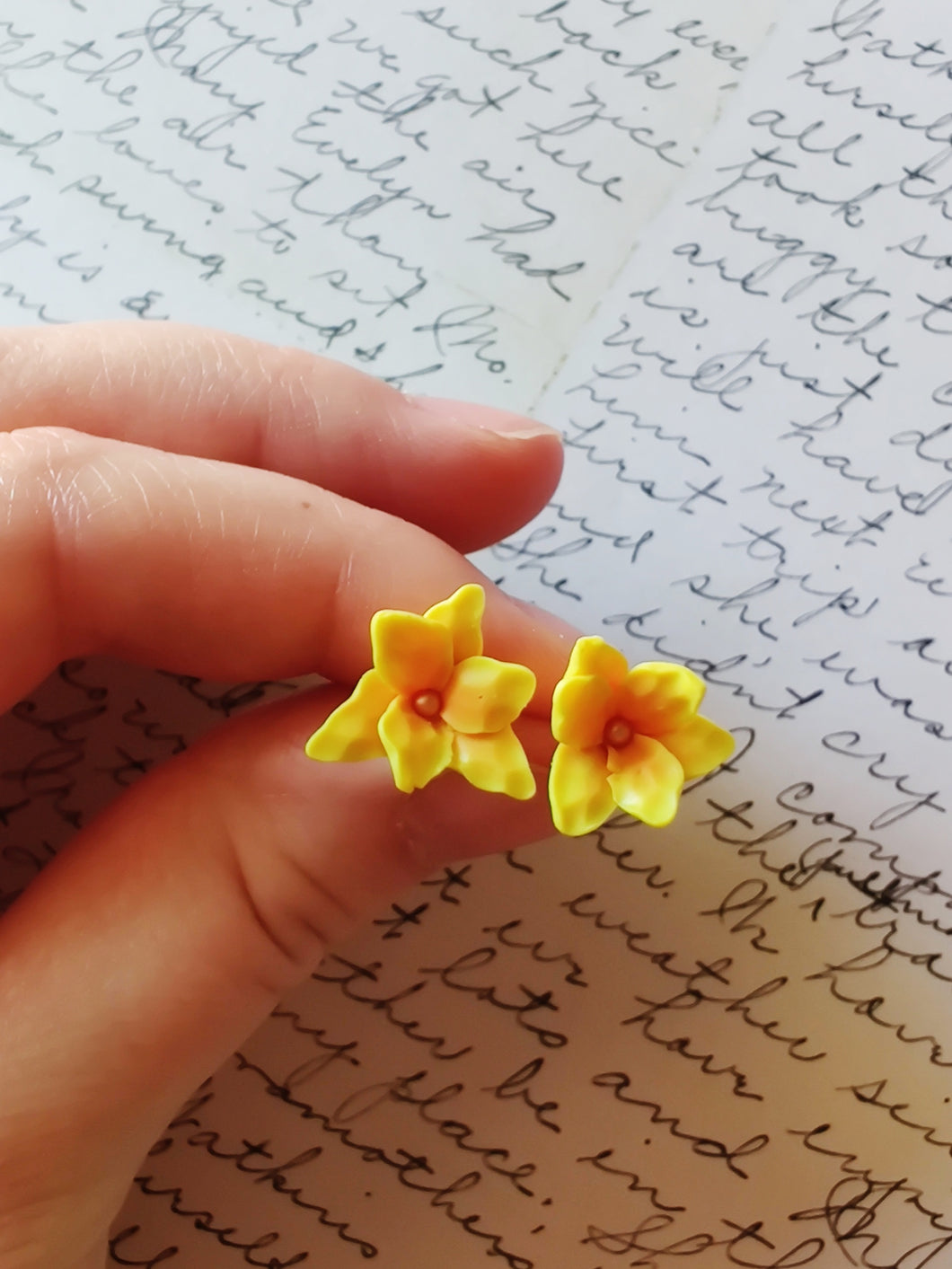 One pair of yellow and orange daylily earrings held between finger and thumb.