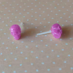 a pair of pink skull shaped earrings displayed on a pale orange and white polka dot background. 