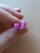 Load image into Gallery viewer, A pair of pink skull shaped earrings held between finger and thumb. 
