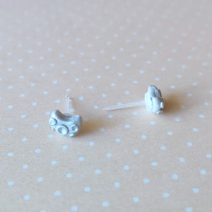 A pair of silver metallic crescent moons with 3D craters on the surface displayed on a pale orange background with white polka dots. 