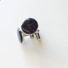 Load image into Gallery viewer, A pair of silver colored cufflinks with a bezel on top. The bezel is filled with polymer clay with a shiny gloss finish. The clay is dark blue with veins of gold, purple, and glow in the dark clay radiating from the center. 
