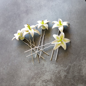 A set of five medium sized white lily hair pins on a mottled grey background.